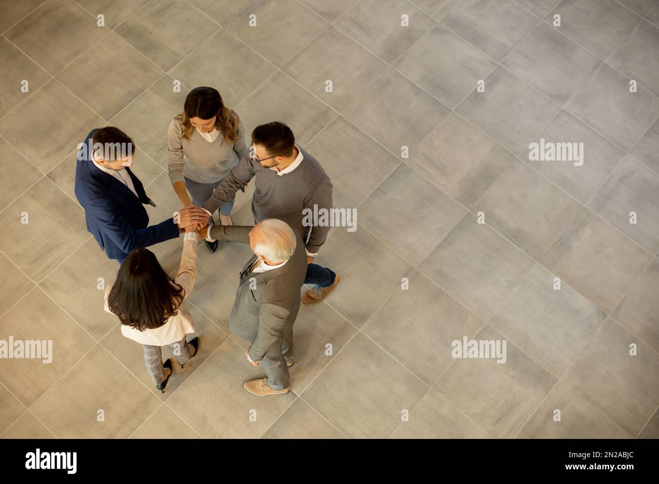 Un groupe de jeunes gens d'affaires et de personnes âgées se réunissent dans un couloir de bureau, debout dans un cercle avec leurs mains jointes. Ils sont habillés de professiono Banque D'Images