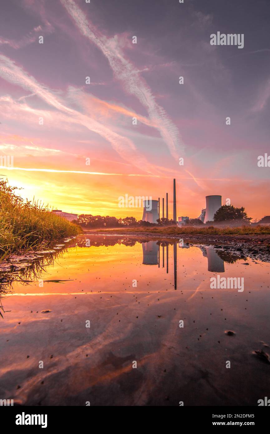 Beau lever de soleil dans un champ, avec une flaque dans le lever du soleil. Contre-jour tourné le matin, en arrière-plan la centrale au charbon Staudinger Banque D'Images