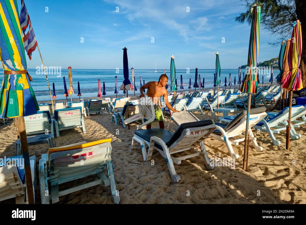 Tôt le matin à Kamala Beach, Phuket, Thaïlande, un homme prépare des chaises longues et des parasols de plage pour les clients attendus Banque D'Images