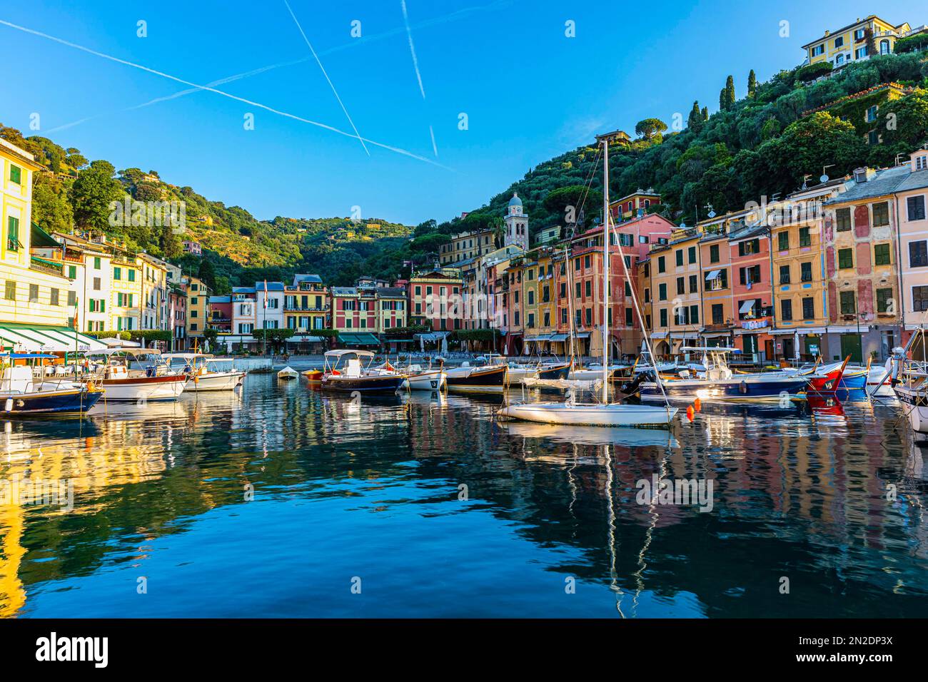 Des bateaux ancholent dans le port de Portofino, derrière eux façades de maisons de couleur pastel de Portofino, pistes de vapeur dans le ciel bleu, Portofino, Ligurie Banque D'Images