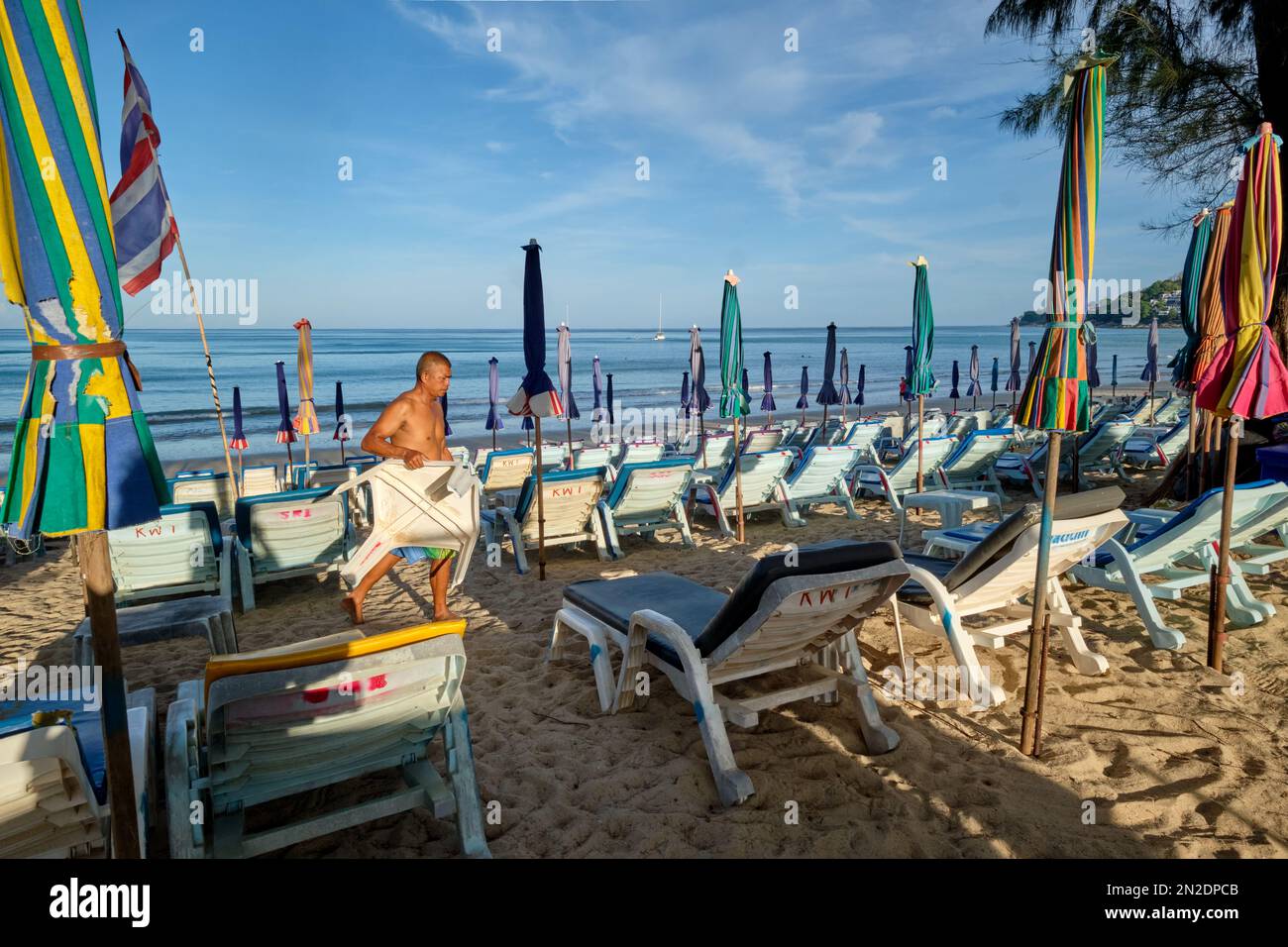 Tôt le matin à Kamala Beach, Phuket, Thaïlande, un homme prépare des chaises longues et des parasols de plage pour les clients attendus Banque D'Images