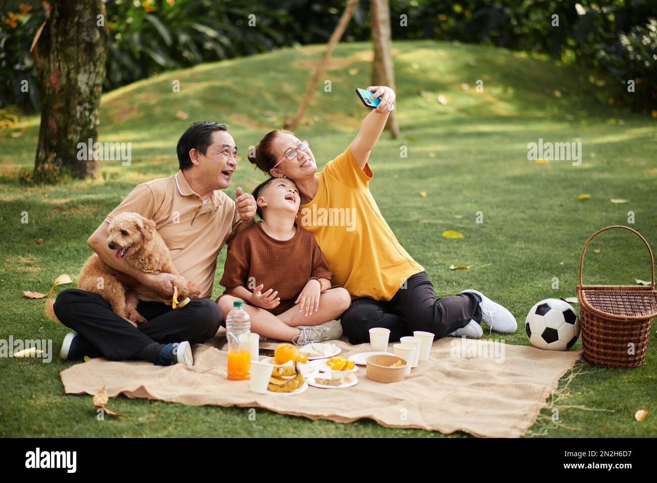 Joyeux grands-parents prenant le selfie avec chien et petit-fils au pique-nique Banque D'Images