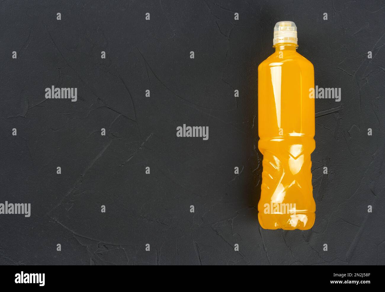 Bouteille en plastique avec boisson isotonique orange pour le sport sur fond de béton foncé. copier l'espace. Banque D'Images