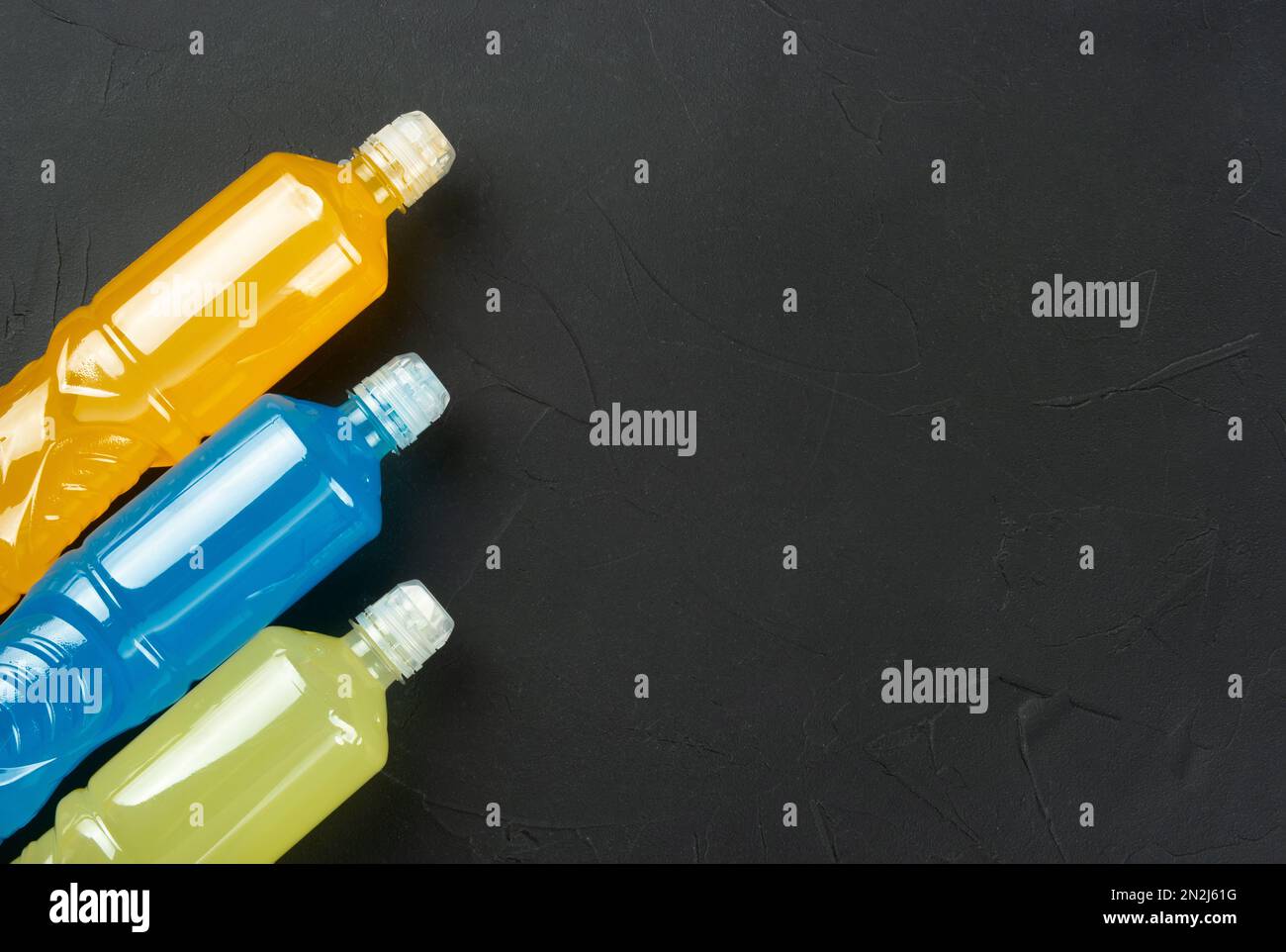 Trois bouteilles en plastique avec boissons isotoniques au citron, à l'orange et au bleu sur fond de béton foncé. copier l'espace. Banque D'Images