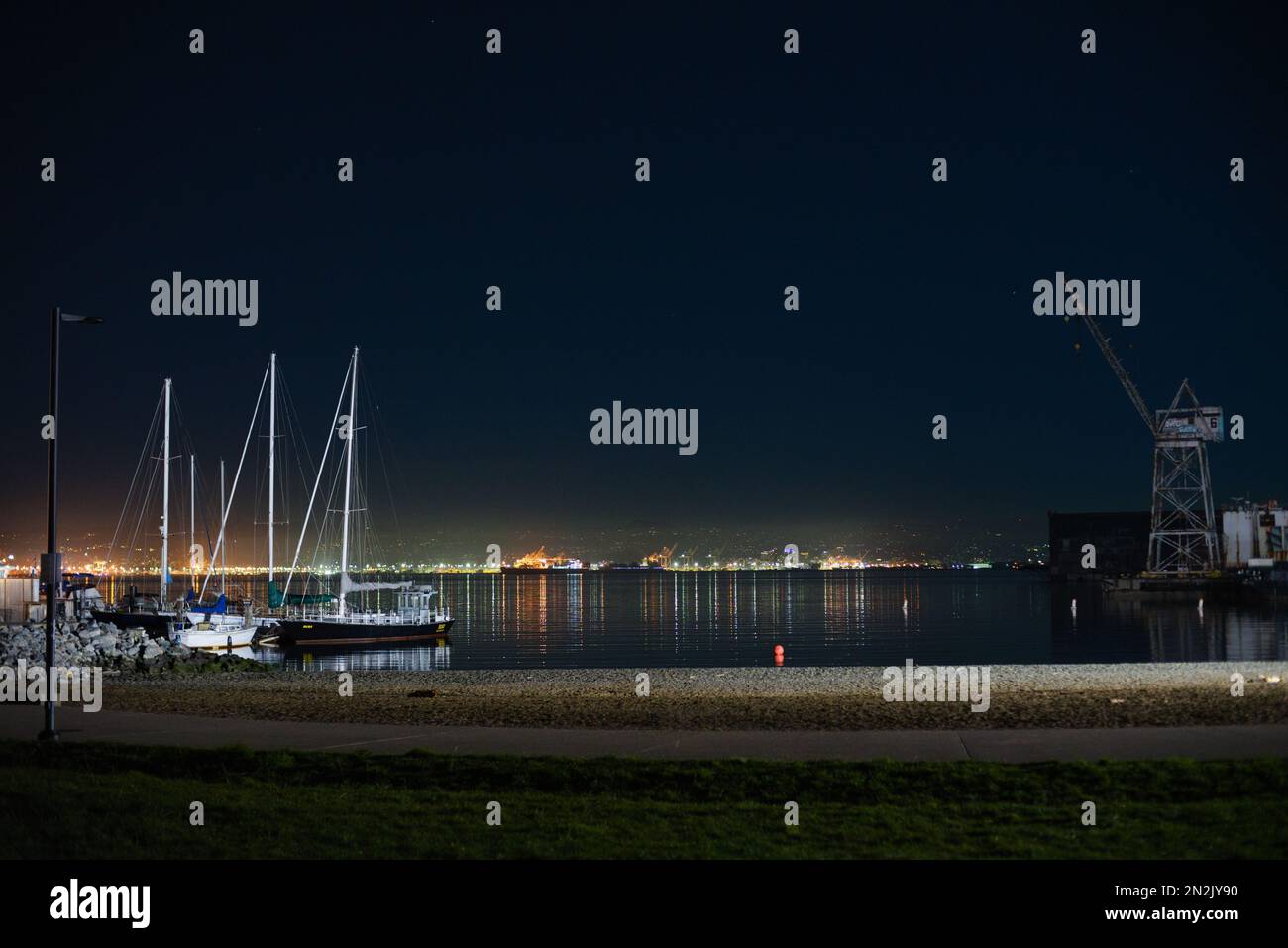 Crane Cove Park la nuit en regardant de l'autre côté de l'eau de la baie de San Francisco sur les lumières de nuit de la ville d'Oakland. Quartier de Dogpatch, San Francisco, États-Unis Banque D'Images