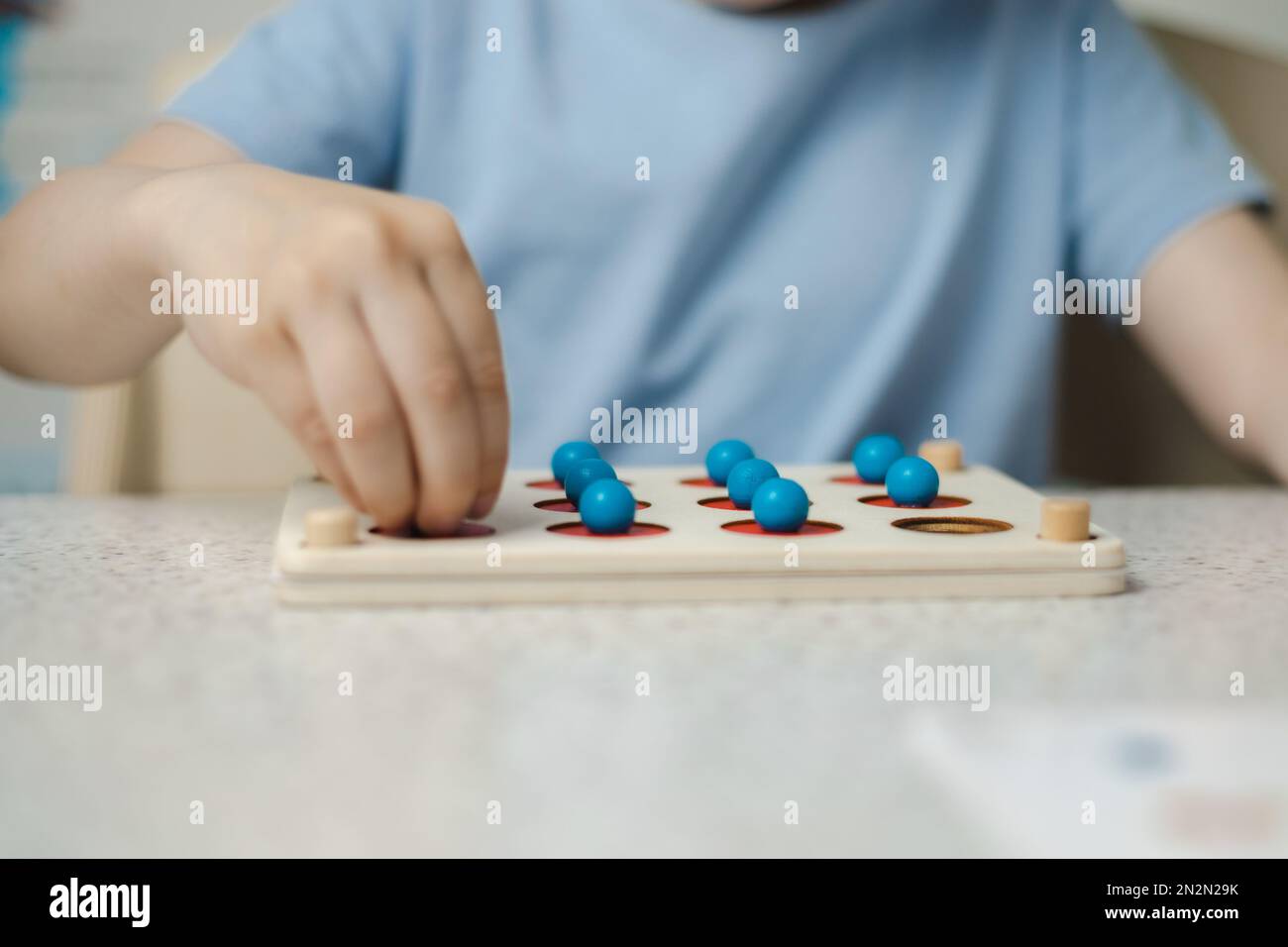 Gros plan des mains d'un enfant méconnaissable jouant un jeu pour le développement de la mémoire et de la pensée. Jouets écologiques en bois Banque D'Images