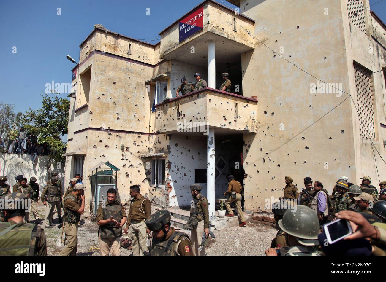Bullet marks from a rebel attack are seen on the walls of Rajbagh police station as security personnel stand at the site in Kathua district, about 80 kilometers (50 miles) south of Jammu, India, Friday, March 20, 2015. Suspected rebels wearing army uniforms stormed the Indian police station in Kashmir, sparking a four-hour gun battle near the border between Indian- and Pakistani-controlled parts of the disputed Himalayan region. (AP Photo/Channi Anand) Banque D'Images