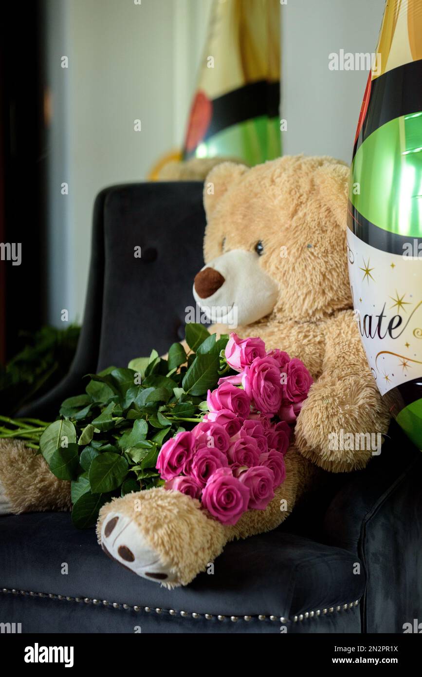 Gros plan d'un ours en peluche avec un bouquet de roses roses et des ballons de champagne Banque D'Images