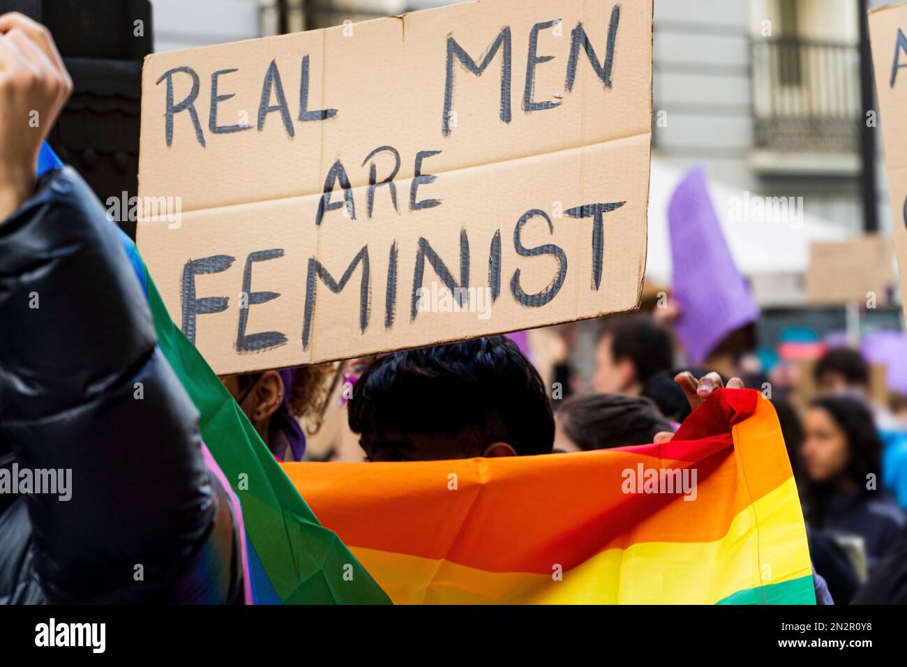 Jeune adulte gay avec drapeau lgbtq et soutien d'un message féministe écriteau sur une manifestation dans la rue Banque D'Images
