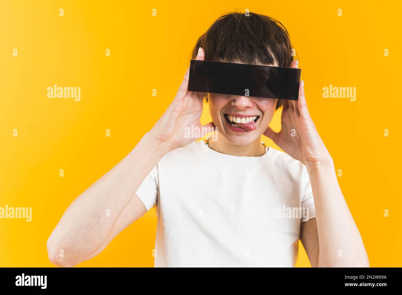 Une personne à la mode qui a l'air folle avec des lunettes de soleil rectangulaires noires sur les yeux qui collent la langue pendant un sourire crasseux. Arrière-plan orange. Photo de haute qualité Banque D'Images