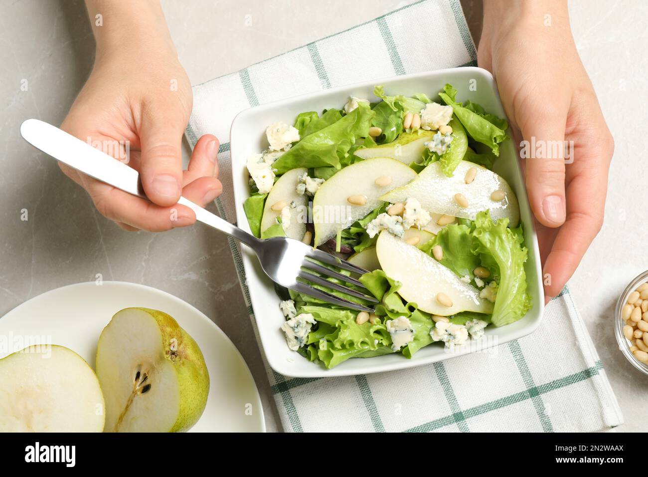 Femme mangeant de la salade fraîche avec des poires à la table lumineuse, vue de dessus Banque D'Images