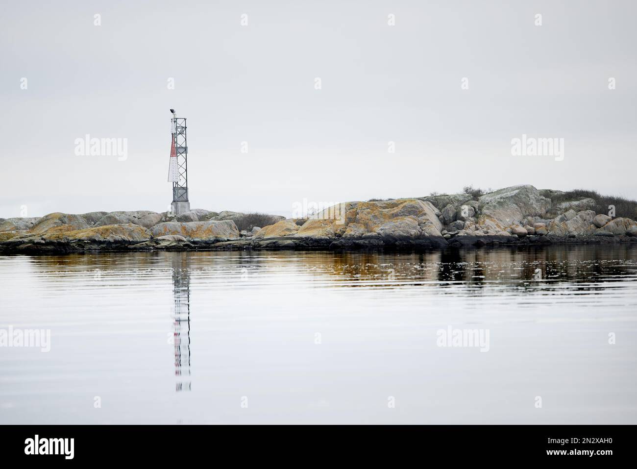Une petite maison de lumière sur un scaur au bord de la côte avec son reflet dans la surface calme de l'eau Banque D'Images