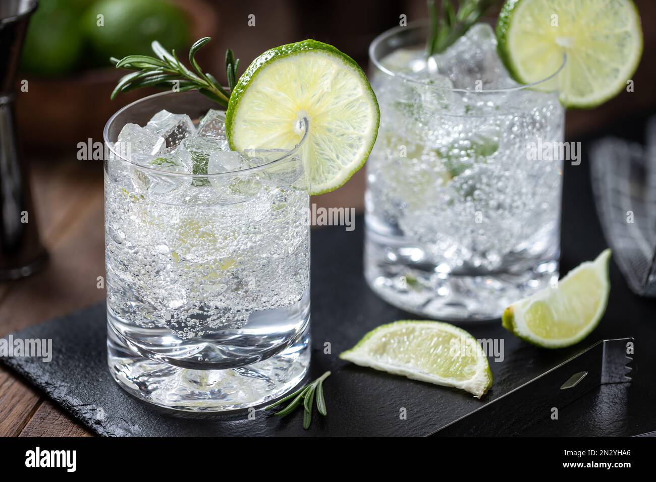 Boisson gazeuse et tonique avec tranches de citron vert, romarin et glace sur un panneau d'ardoise noir Banque D'Images
