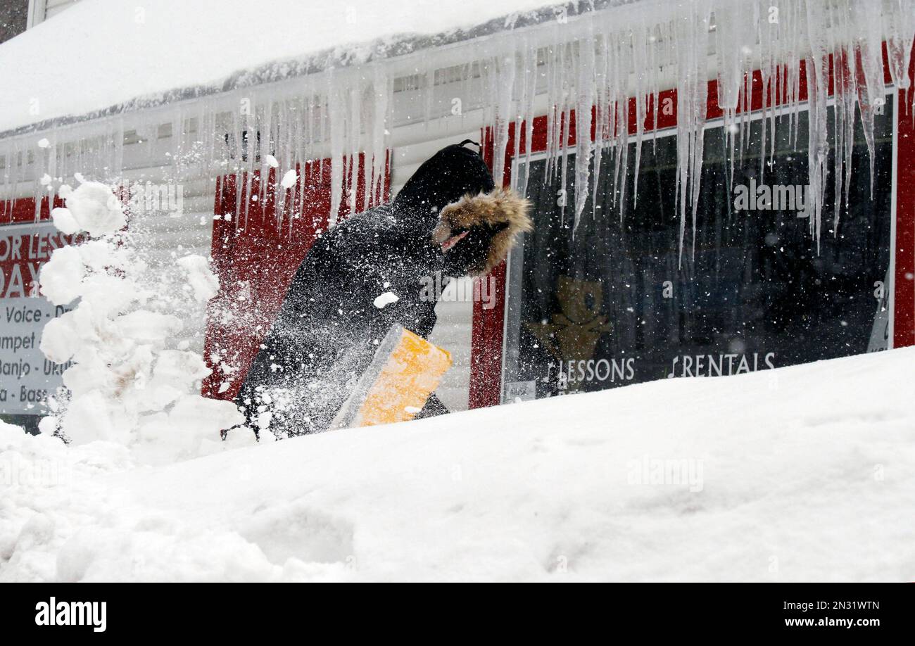 Corbit Larson clears snow in front of icicles hanging off his Centre Music store, Monday, Feb. 9, 2015, in Framingham, Mass. A long duration winter storm that began Saturday night remains in effect for a large swath of southern New England until the early morning hours Tuesday. (AP Photo/Bill Sikes) Banque D'Images
