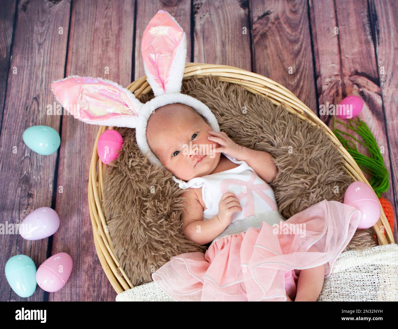 Bébé fille nouveau-né dans le panier de Pâques portant des oreilles de lapin. Banque D'Images