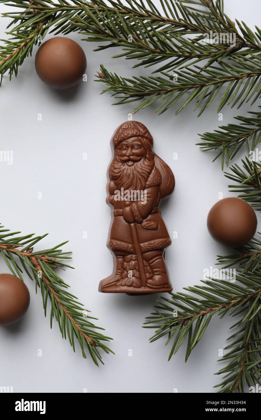 Composition de la couche plate avec le Père Noël en chocolat, brindilles de sapin et bonbons sur fond blanc Banque D'Images