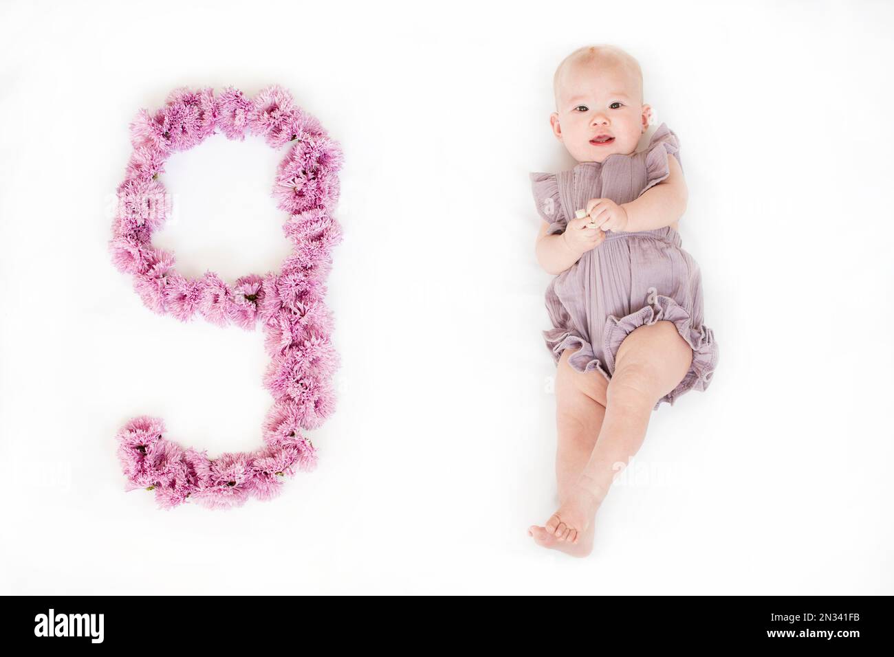 Petite fille de nouveau-né dans une barboteuse pourpre. bébé de 9 mois. Un jalon de neuf mois pour le bébé. Banque D'Images