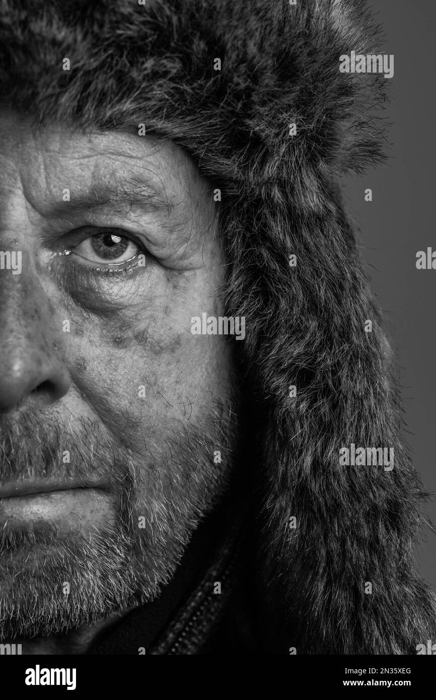 Gros plan demi-visage portrait noir et blanc d'un homme d'extérieur robuste et expérimenté, avec une barbe portant un aviateur de fourrure ou un chapeau de style trappeur Banque D'Images