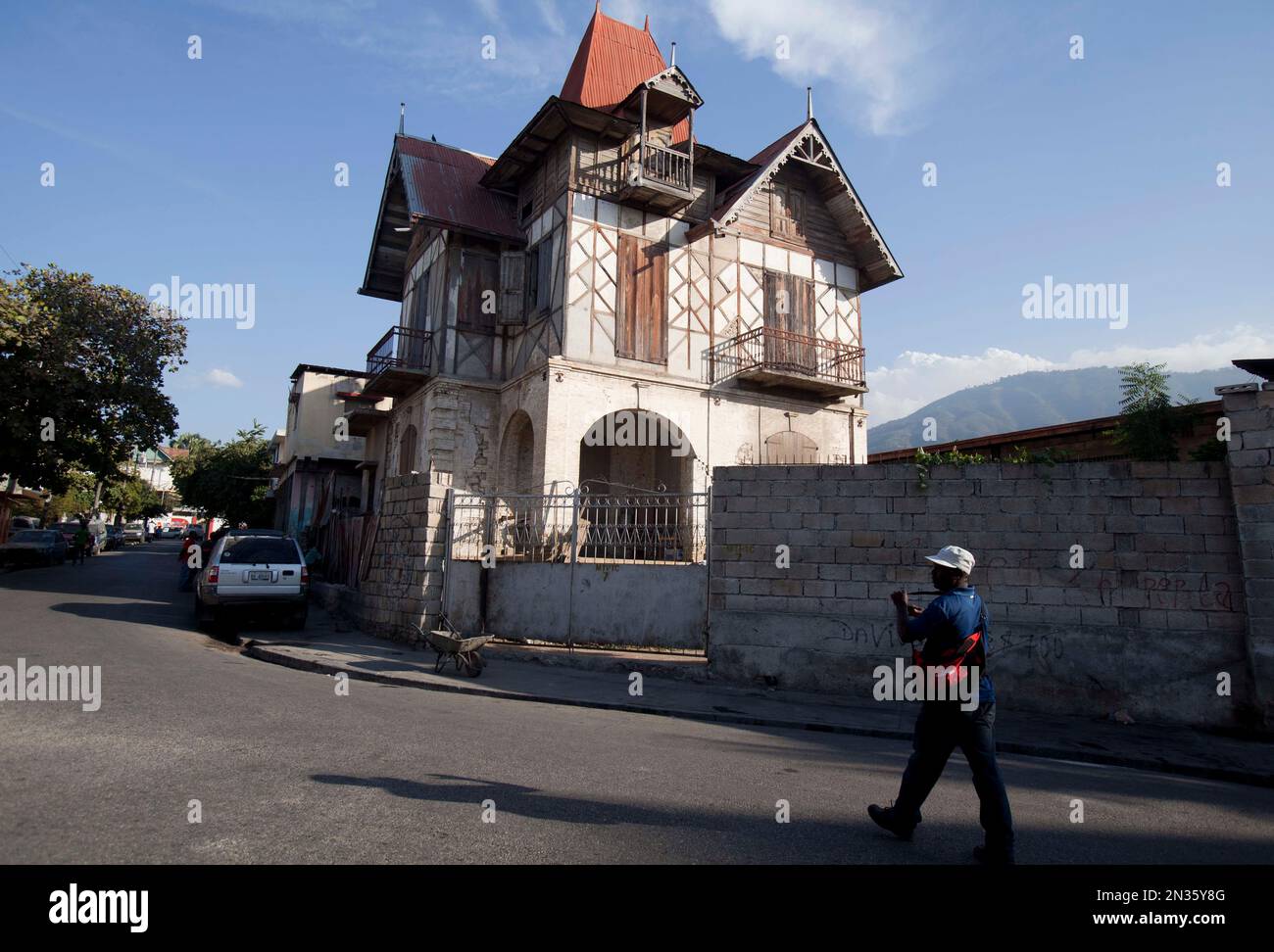 In this Jan. 14, 2015 photo, a man walks next to a "gingerbread house" in Port-au-Prince, Haiti. It wasn’t until the 2010 earthquake devastated Haiti’s capital that many people even realized that dozens of the city’s grandest old buildings were still standing _ its quirky and ornate “gingerbread houses” with their fancy latticework, turrets and spires. (AP Photo/Dieu Nalio Chery) Banque D'Images