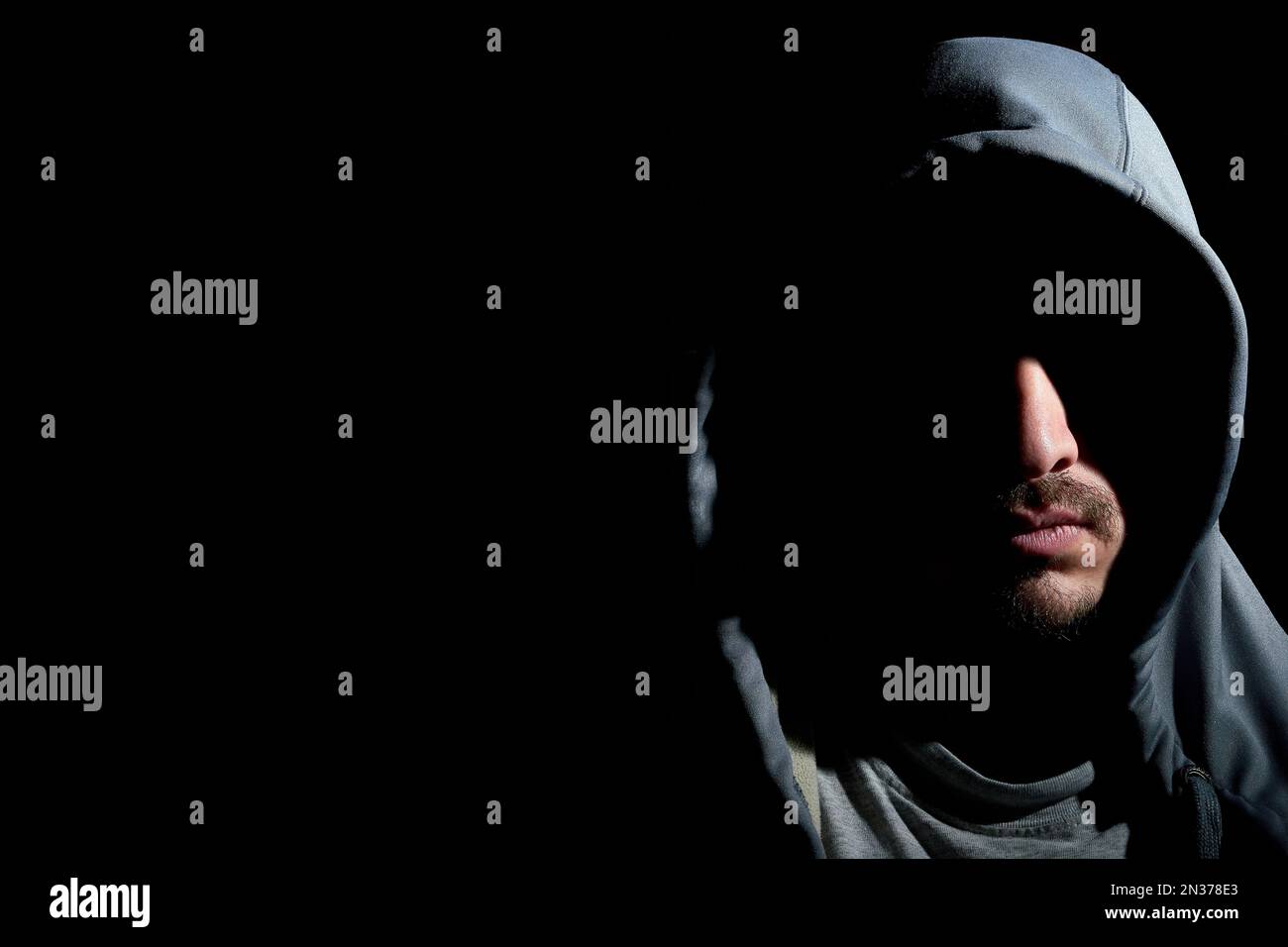 Portrait horizontal d'un mystérieux jeune homme à capuchon barbu avec son visage recouvert d'ombres isolées sur fond noir foncé avec espace de copie. St Banque D'Images