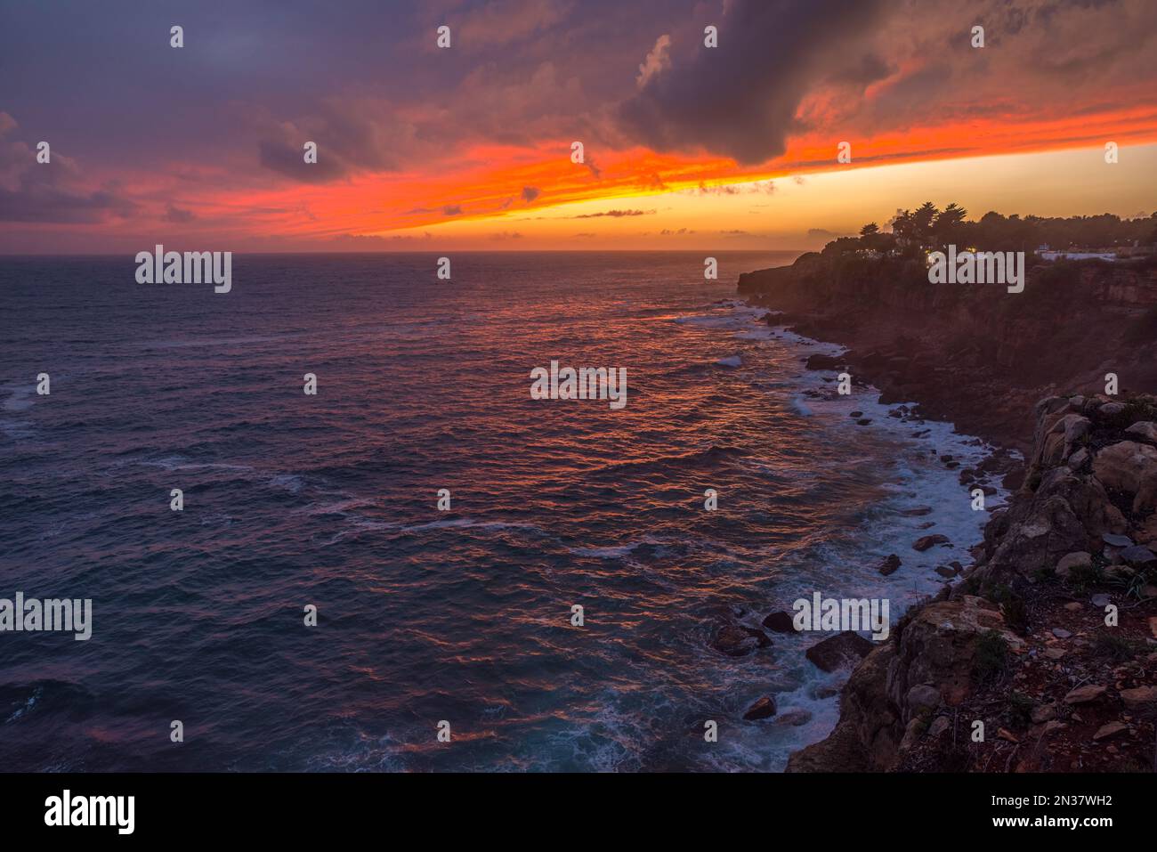 Coucher de soleil rouge coloré et ciel spectaculaire vif sur la rive rocheuse de l'océan Atlantique. Banque D'Images