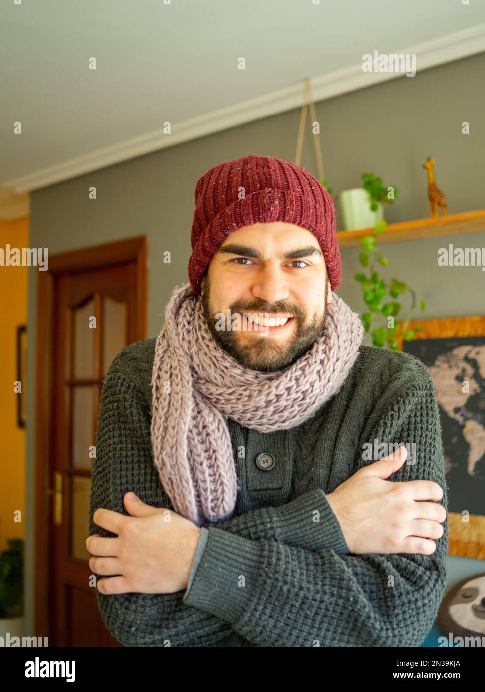 Jeune homme barbu portant, écharpe et chapeau d'hiver pour combattre la  vague de froid dans un salon confortable. Regarder l'appareil photo Photo  Stock - Alamy