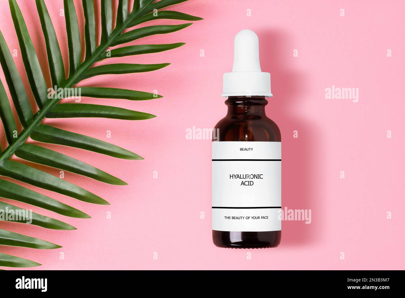 Acide hyaluronique dans un pot à cosmétiques brun en verre. Avec une inscription. Sur fond rose. Avec feuille de palmier. Banque D'Images
