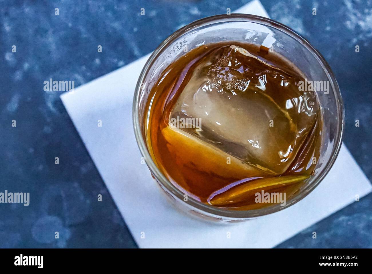 Whisky dans un verre avec cube de glace sur table avec serviette blanche, vue de dessus, Banque D'Images