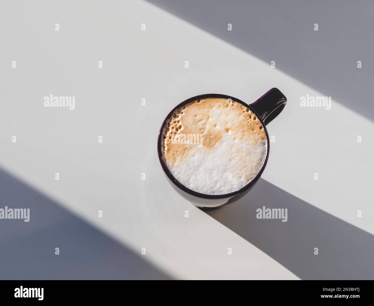 Vue de dessus sur une tasse de cappuccino. Fond géométrique minimaliste avec tasse à café. Lumière, ombre et boisson chaude avec mousse de lait sur table blanche. Banque D'Images