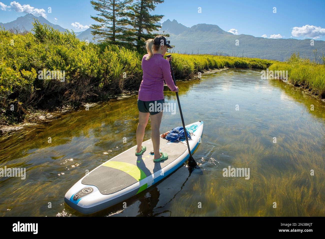 Vue de derrière d'une femme caucasienne paddle board à Rabbit Slough, vers Twin Peaks dans les montagnes Chugach, par une journée ensoleillée d'été avec un ... Banque D'Images