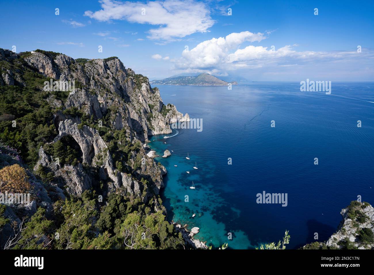 Vue depuis les falaises rocheuses de l'île de Capri sur la côte amalfitaine et la baie de Naples avec des bateaux amarrés au large du rivage Banque D'Images