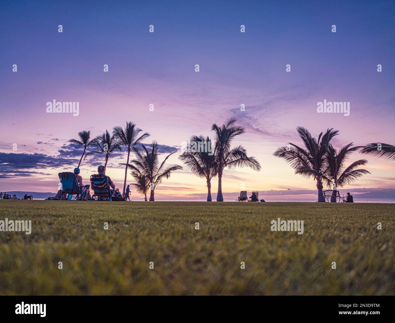 Vue prise de l'arrière des touristes assis dans des chaises longues regardant le coucher de soleil sur la côte Pacifique à Makena; Maui, Hawaii, États-Unis d'Amérique Banque D'Images