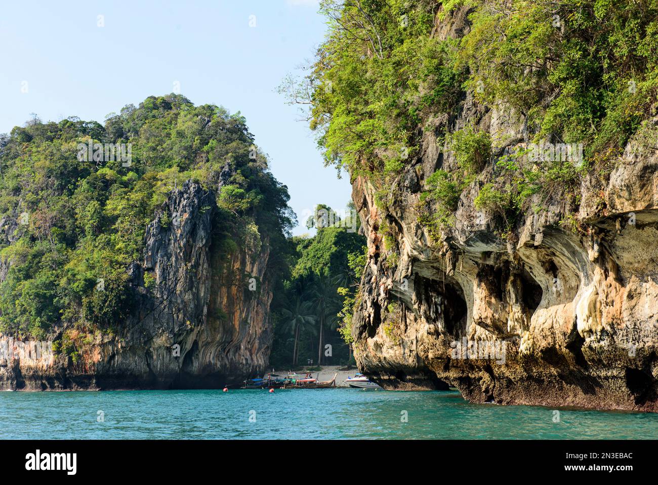 Vue sur les formations rocheuses et les falaises le long de la rive d'une petite baie avec des bateaux amarrés à la plage sur une île tropicale ; Phang Nga Bay, Thaïlande Banque D'Images