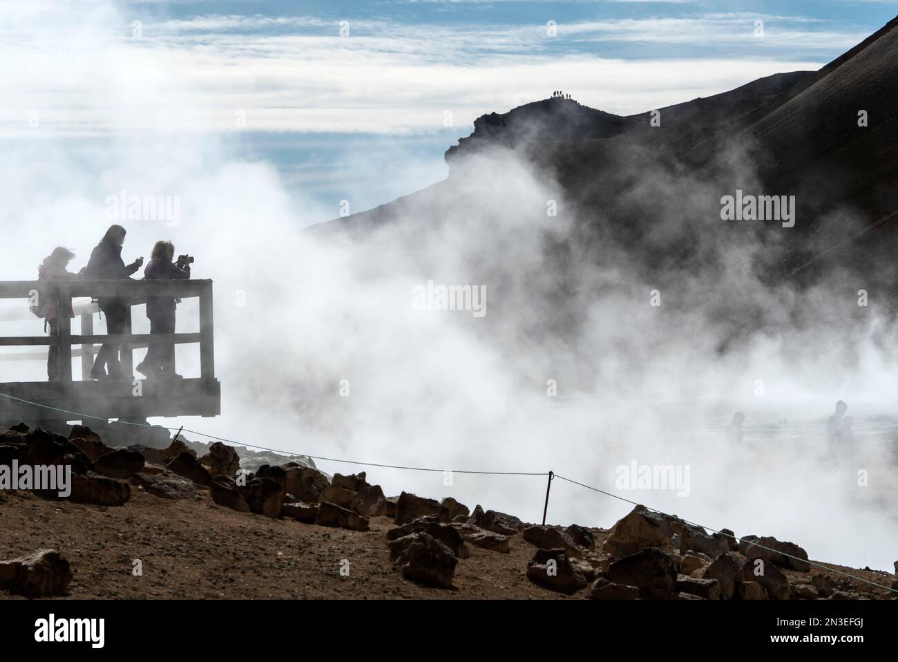 Les personnes se tenant sur la plate-forme d'observation surplombant et prenant des photos du lac Myvatn, entouré par la vapeur qui s'élève des évents géothermiques. L... Banque D'Images