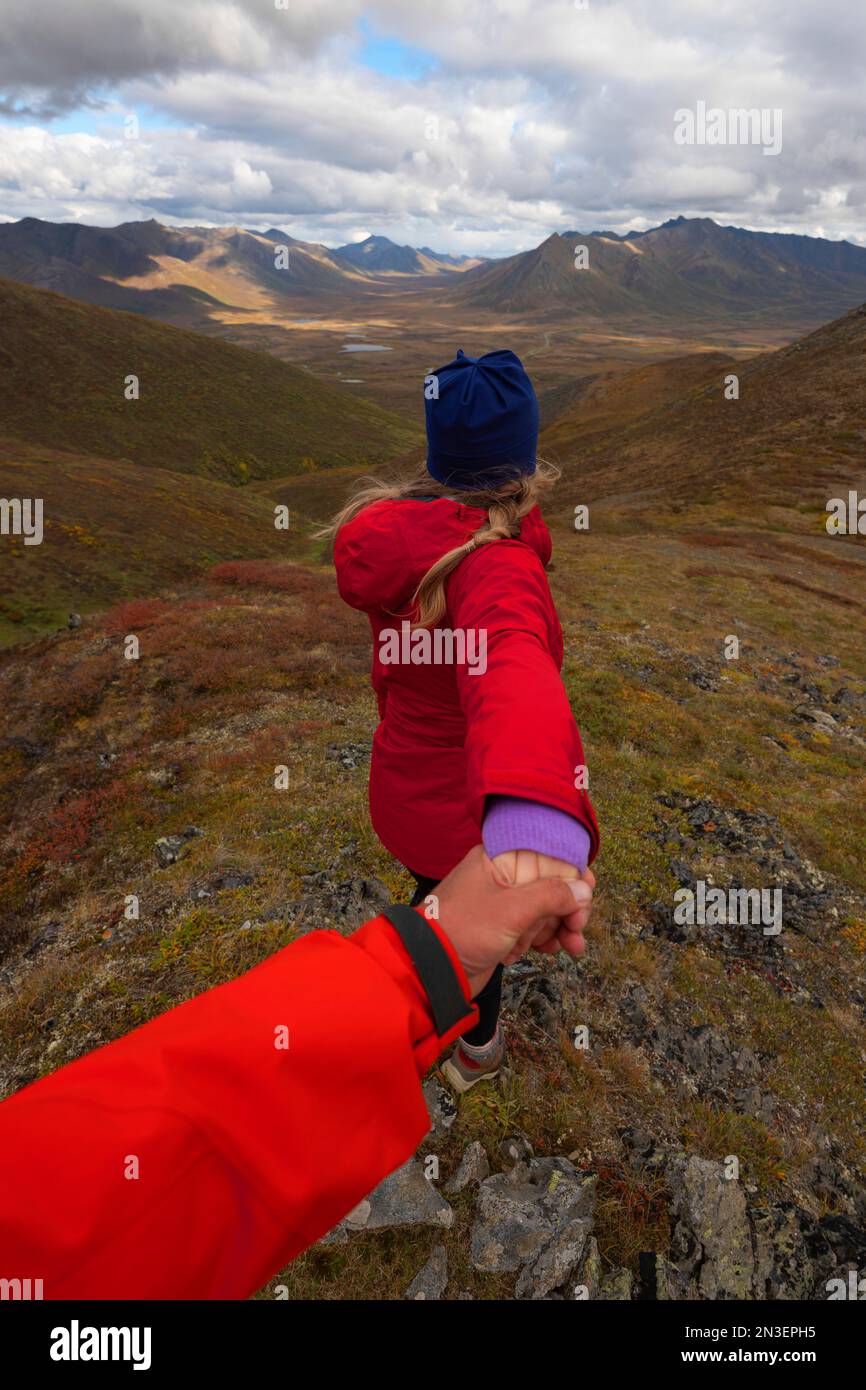 Vue prise de derrière d'une femme randonneuse prenant un homme randonneur par la main au sommet d'une montagne le long de la route Dempster ; Dawson City, Yukon, Canada Banque D'Images