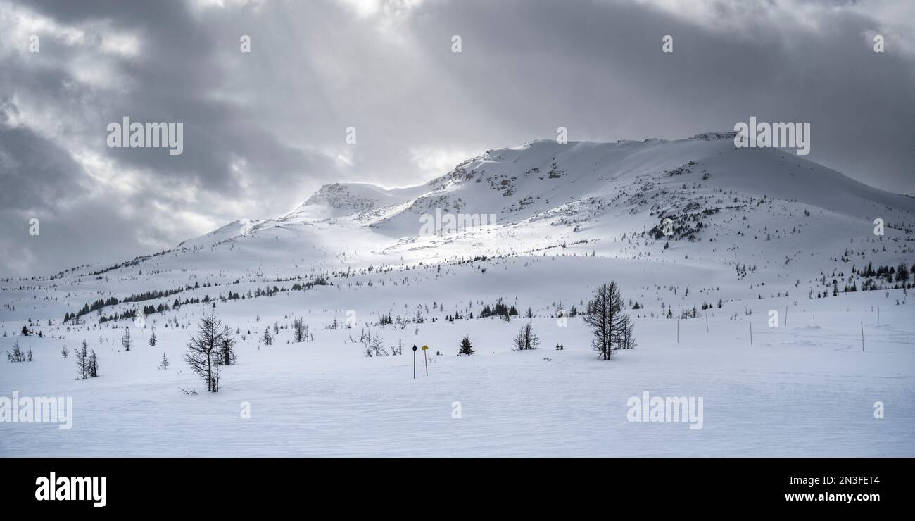 La lumière du soleil brille à travers les nuages jusqu'aux montagnes Rocheuses enneigées dans une station de ski du parc national Banff, Alberta, Canada Banque D'Images