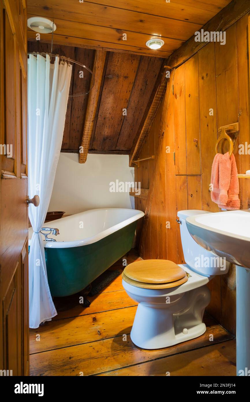 Salle de bains avec baignoire de 1880s pieds de griffe verte, toilettes avec siège en bois et lavabo sur pied à l'étage à l'intérieur de la vieille maison Canadiana vers 1750. Banque D'Images