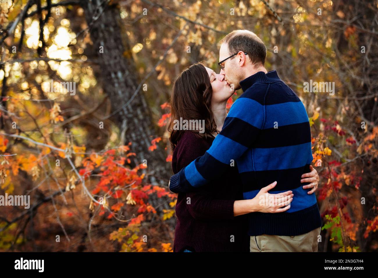 Un couple marié mature s'embrasse tout en passant du temps ensemble à l'extérieur dans un parc de la ville pendant la saison d'automne; St. Albert, Alberta, Canada Banque D'Images