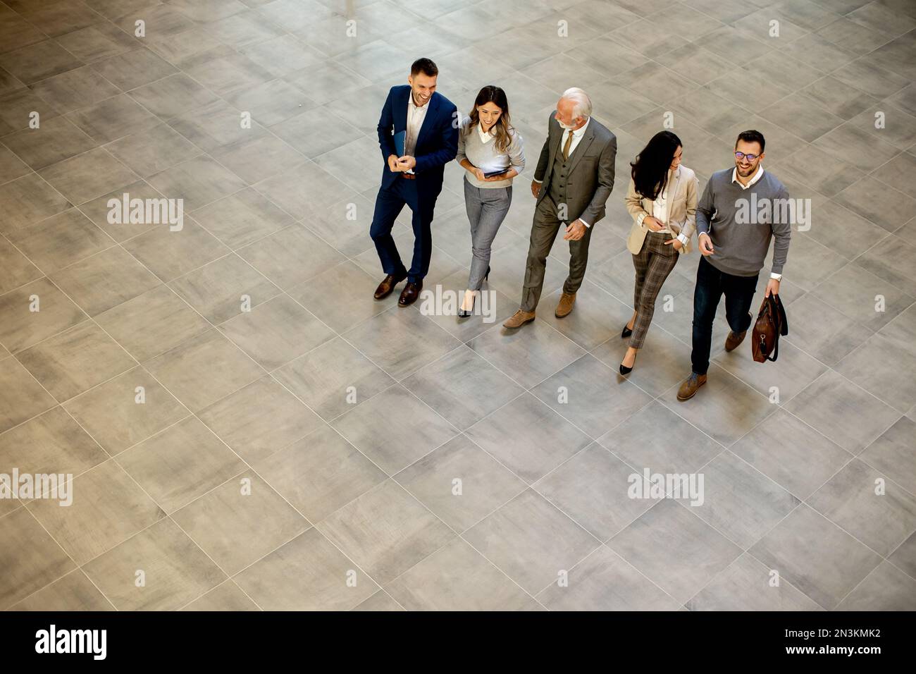 Un groupe de jeunes et de personnes âgées en voyage d'affaires se prompe dans un couloir de bureau, capturé dans une vue aérienne. Ils sont vêtus d'une tenue habillée, ils marchent avec humour Banque D'Images