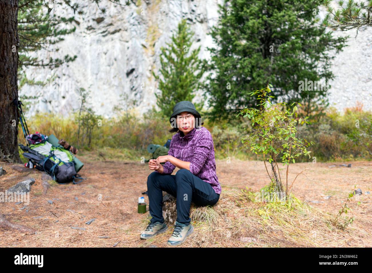 Une fille de voyageur asiatique dans un chapeau et des lunettes se trouve sur une pierre près des choses touristiques dans la forêt. Banque D'Images