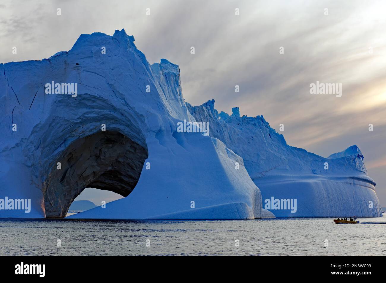 Grand iceberg avec trou, petit bateau devant lui, minuit, été dans l'Arctique, Ilulissat, Disko Bay, Amérique du Nord, Groenland, Danemark Banque D'Images