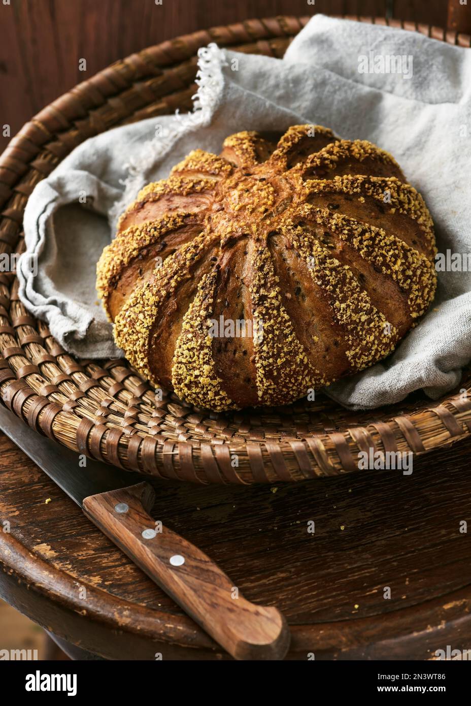 Pain rond savoureux d'orge et de farine de maïs fraîchement cuits avec serviette en tissu dans un panier en osier sur un vieux tabouret en bois d'époque. Aliments sains faits maison Banque D'Images
