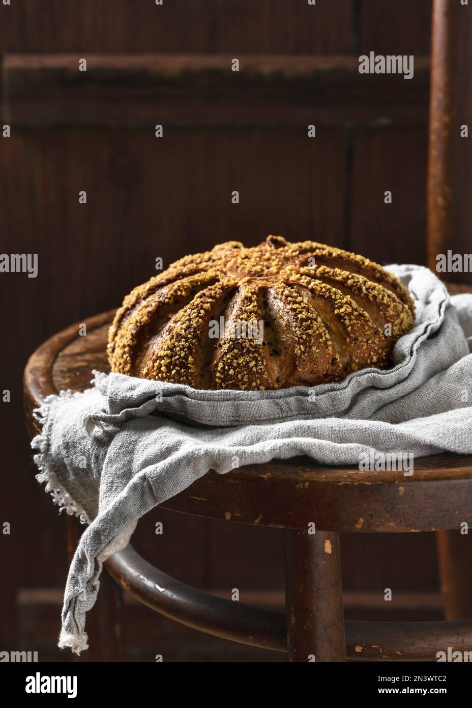 Encore plus de vie avec du pain rond fraîchement cuit, de l'orge et de la farine de maïs avec une nappe de linge de maison sur une chaise en bois vintage. Style rustique sombre. Banque D'Images