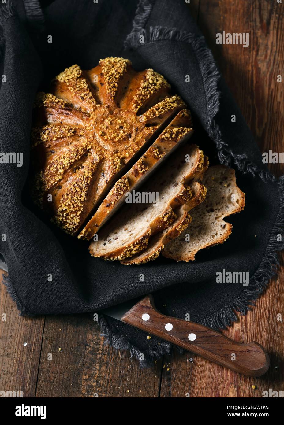 Vue de dessus de tranches d'orge wholegrain et de pain de maïs sur une serviette en toile de lin sombre avec couteau sur fond de bois rustique. Copier l'espace. Banque D'Images