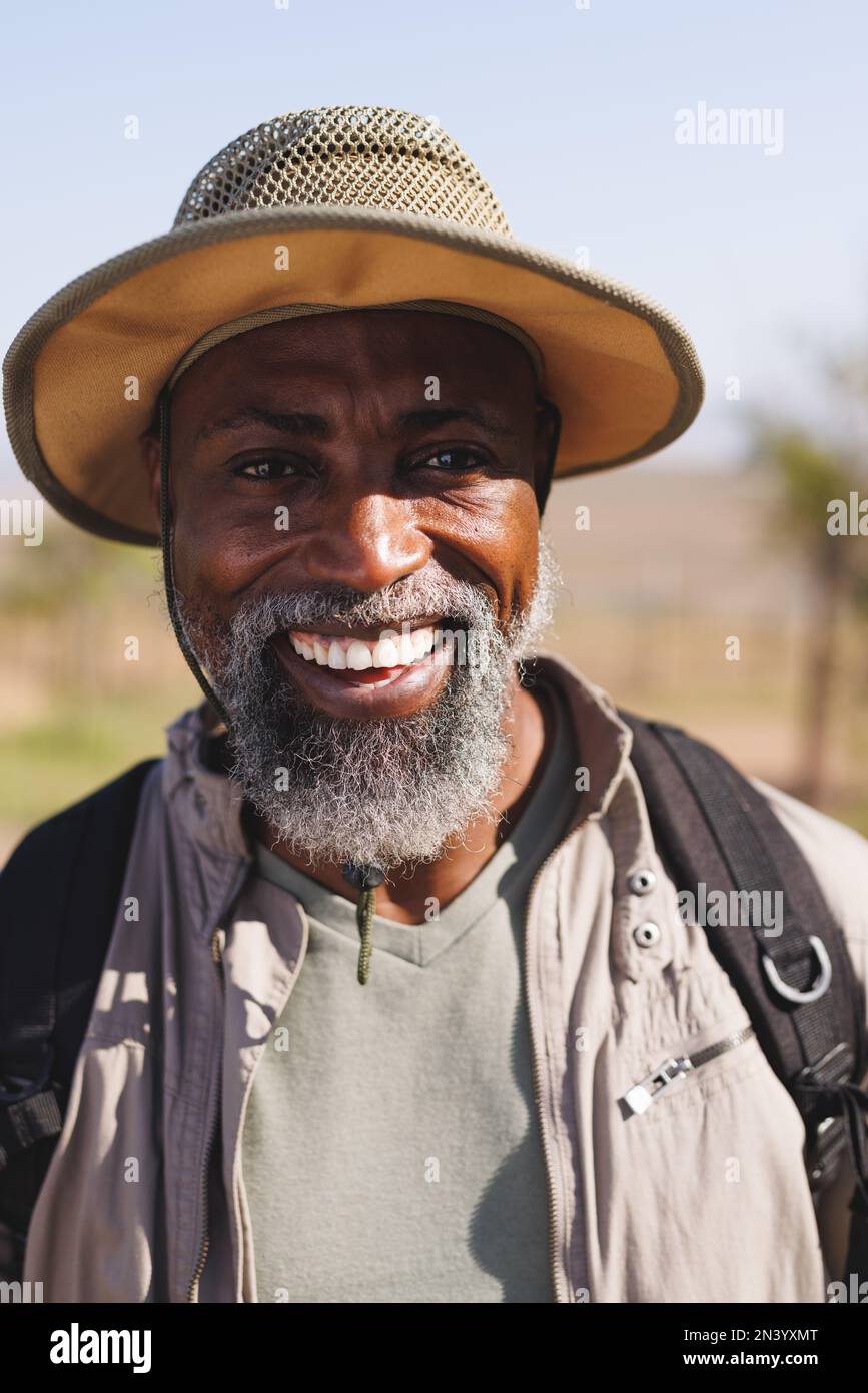 Portrait en gros plan d'un homme senior afro-américain à barbe souriante portant un chapeau en randonnée dans un ciel dégagé Banque D'Images