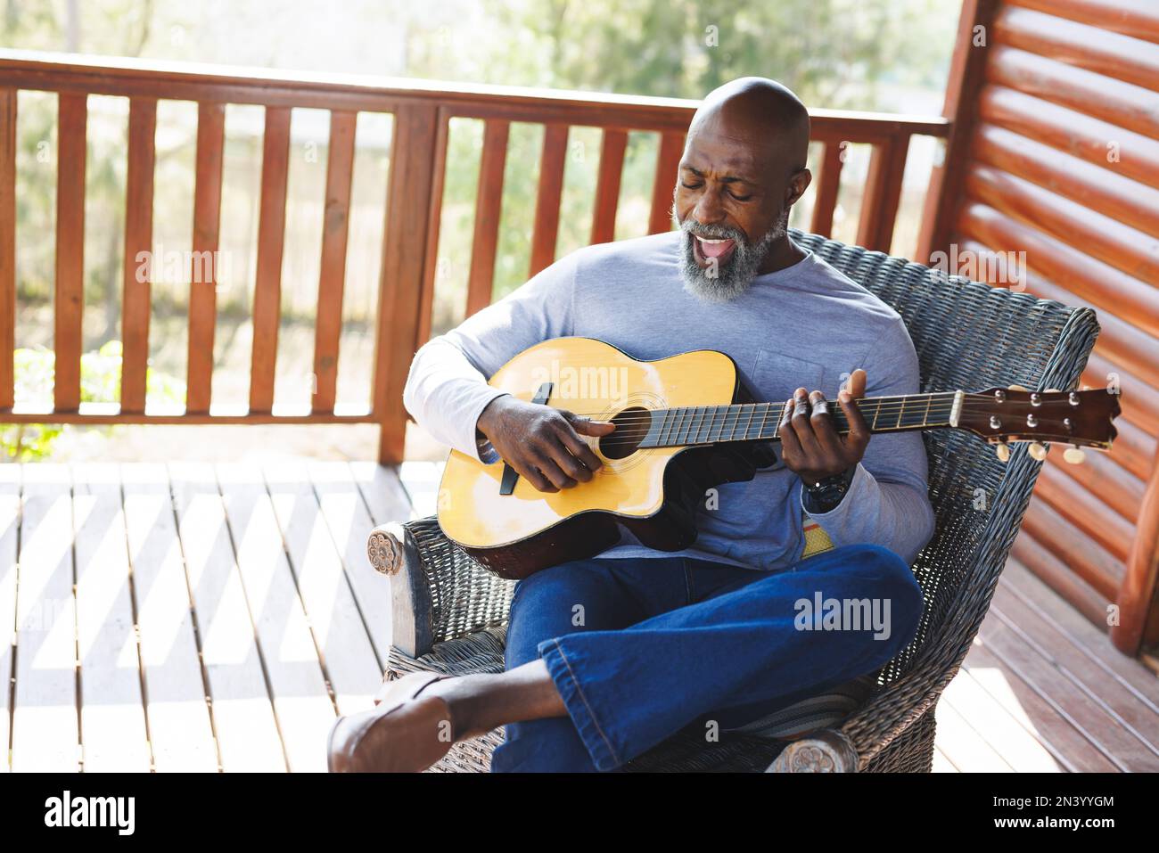 Chauve african american senior homme chantant et jouant de la guitare tout en étant assis sur une chaise sur le balcon Banque D'Images