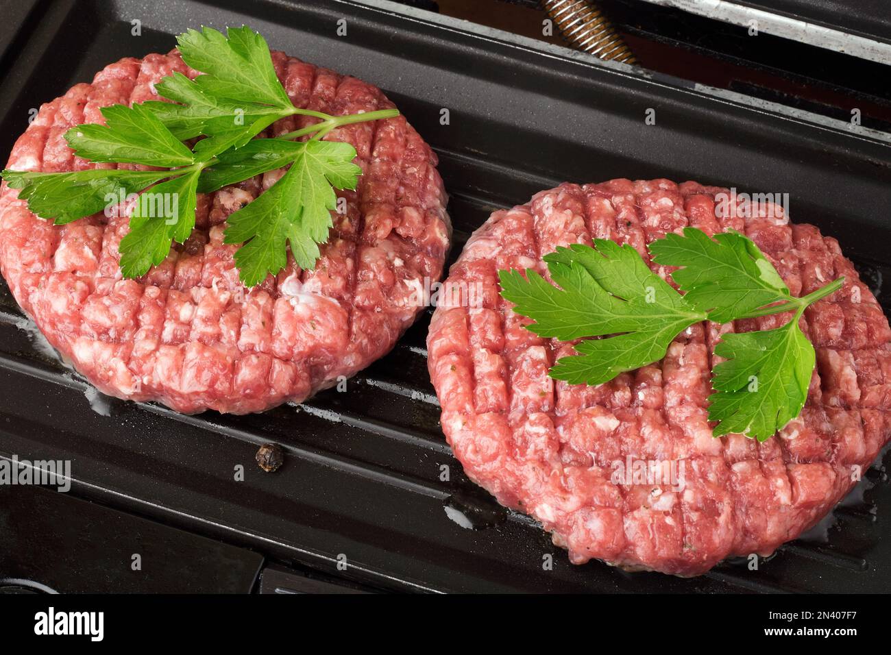 Viande de boeuf haché cru steak côtelettes hamburger frites sur un gril chaud. Côtelette pour hamburger avec légumes et épices. Banque D'Images