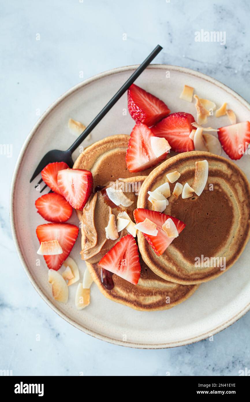 Crêpes végétaliennes avec fraises, beurre de noix, chips de noix de coco et sirop, vue du dessus. Banque D'Images