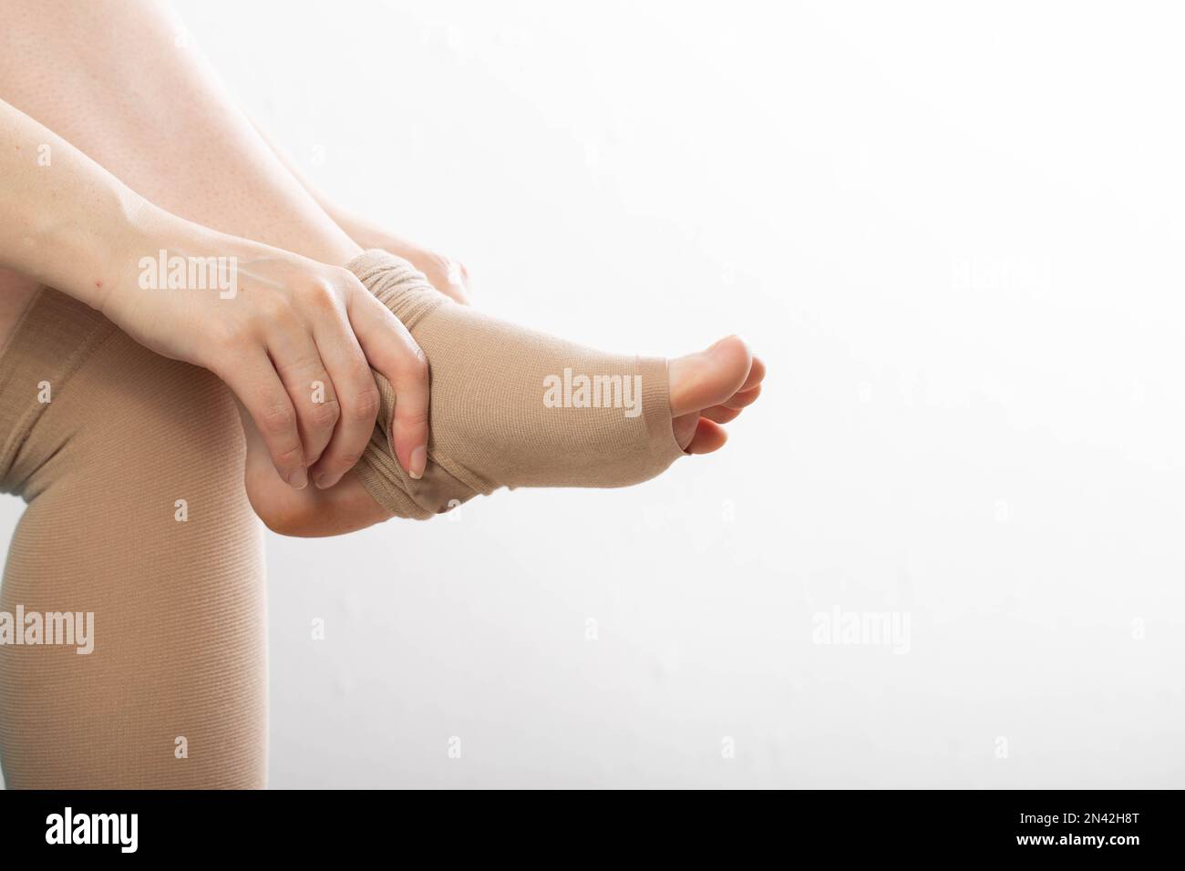 Une femme enceinte met sur ses jambes des bas de contention pour les varices. Arrière-plan blanc. Grossesse et varices, phlébologie, thrombus Banque D'Images