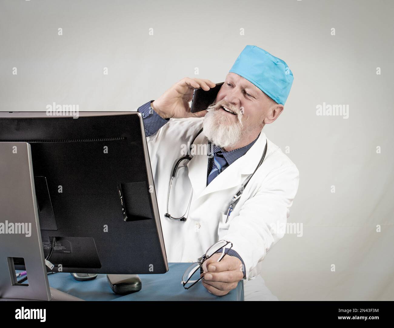 Cabinet médical.médecin âgé positif parlant sur smartphone devant l'ordinateur. Banque D'Images